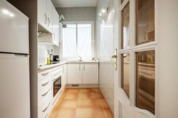 Крытая кухня с белыми деревянными шкафами, белая деревянная столешница, черная керамическая плита, микроволновая печь, масленка и мелкая бытовая техни