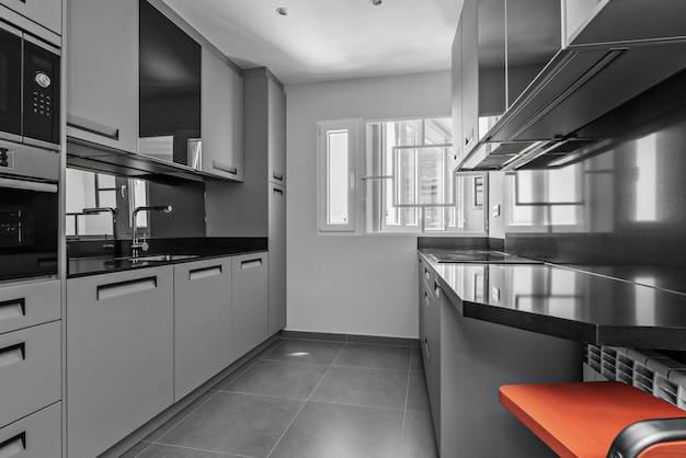 Изображение кухни с серыми деревянными шкафами, гармонирующими с полом, столешницей из черного камня и черной встроенной техникой