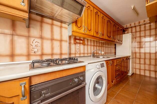 Кухня со столешницей из искусственного мрамора кремового цвета и оранжево-коричневой плиткой, деревянными шкафами в деревенском стиле и встроенной бытовой техникой