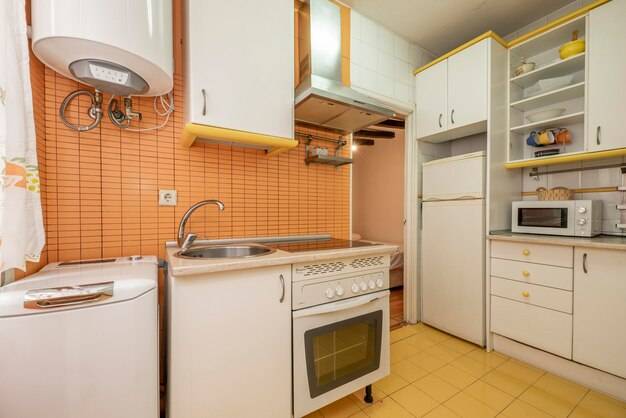 Дешевая кухня с белой мебелью и желтыми деталями, сломанными приборами и керамогранитными полами