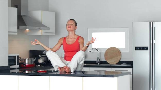 Молодая женщина расслабляется в медитации йоги в позе лотоса во время приготовления пищи на кух