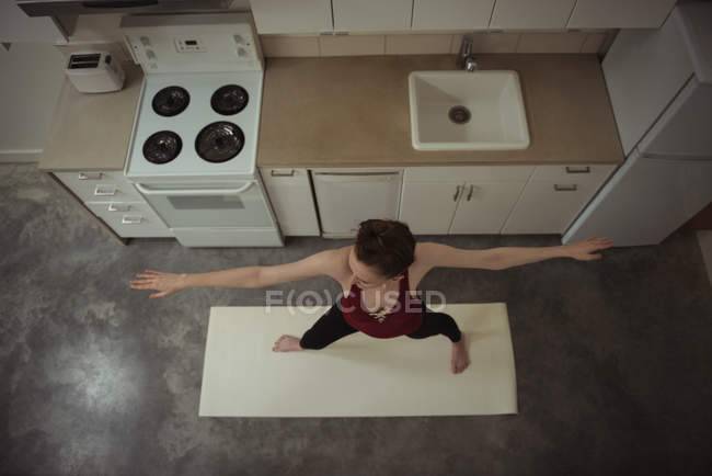 Высокоугольный вид женщины, выполняющей растягивающую позу йоги на кухне дом