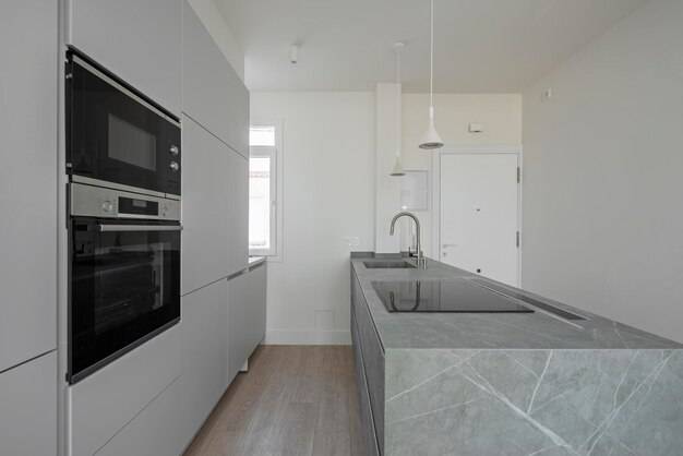 Современная кухня со стеной, покрытой серыми шкафами, черной микроволновой печью и духовкой и зеленым мраморным островом с керамической плитой и раковиной
