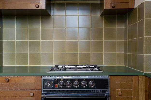Интерьер старой ретро винтажной кухни с антикварной духовкой с коричневыми деревянными шкафами, зеленой старой школьной стильной плиткой, нуждается в ремонте рядом с
