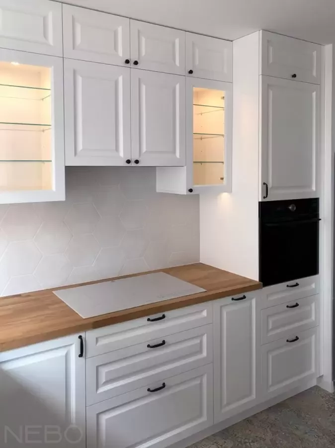 Белая кухня в классическом стиле с фрезерованными фасадами, витринами из стекла, столешницей из массива дуба и черными матовыми ручками