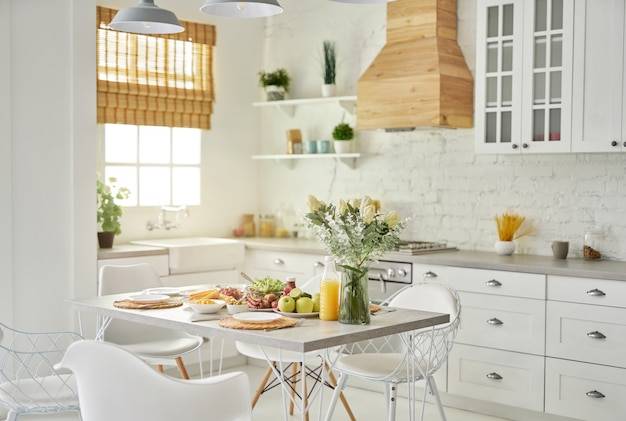 Уютная кухня в современном ярко-белом интерьере кухни с деревянными и белыми деталями ваза с цветами