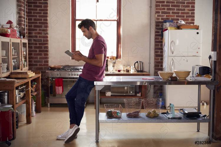 Молодой человек с помощью планшетного компьютера на кухне, полная дли