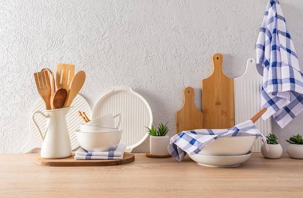 Кухонная утварь и посуда на деревянной столешнице напротив серого цементного интерьера интерьера современной кухни в светлых тонах