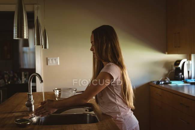 Девушка, стоящая на кухне и моющая руки под водопроводной водой дом