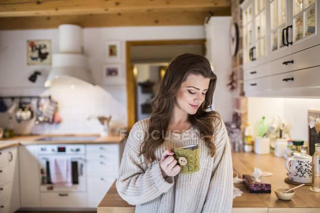 Молодая женщина дома держит чашку кофе на кух