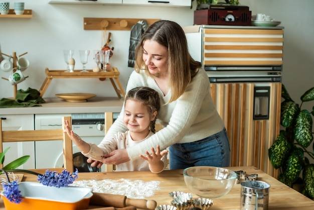 Девушка и женщина готовят дома на кухне ребенок размешивает муку, месит тесто на столе вручную