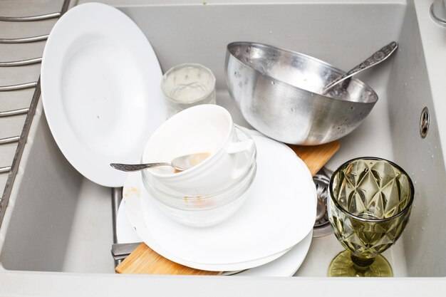 Куча грязных тарелок, таких как столовые приборы тарелок в серой современной гранитной раковине на кух