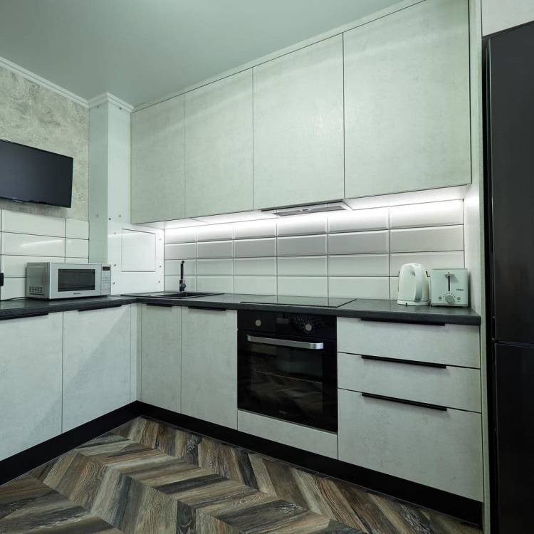 Белая угловая кухня с высокими шкафами и черной столешницей