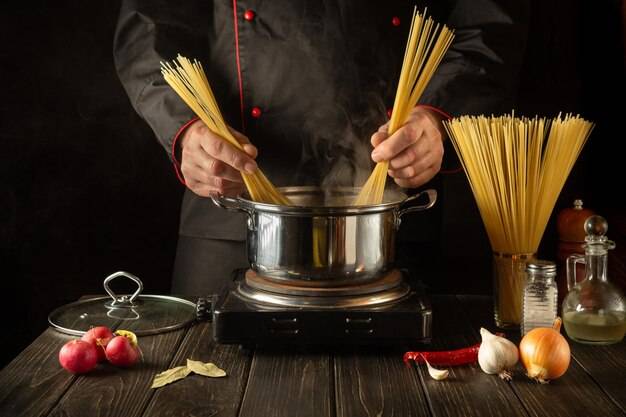 Профессиональный повар готовит суп из спагетти в кастрюле на кух