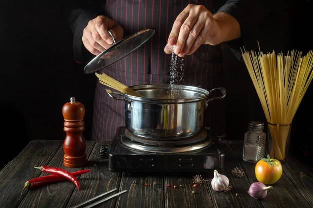 Шеф-повар солит органическую пасту в горячей кастрюле на кухне рецепт вкусной еды в отеле традиционная итальянская кухня