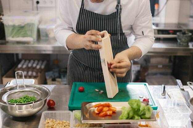 Подготовка овощей для вкусного блюда из миски шеф-повара-мужчины на современной кухне рестор