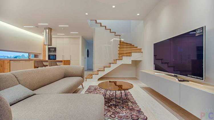 Светло-бежевый интерьер гостиной с кухней и деревянной лестницей на второй этаж